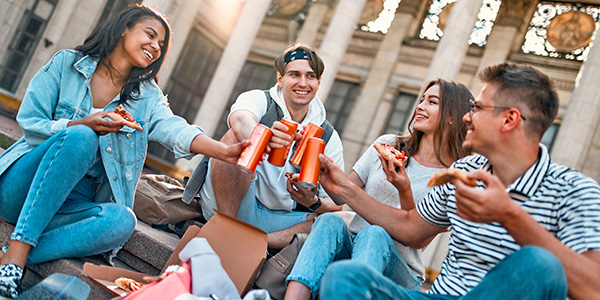 Group of students laughing and cheering drinks together with snacks.